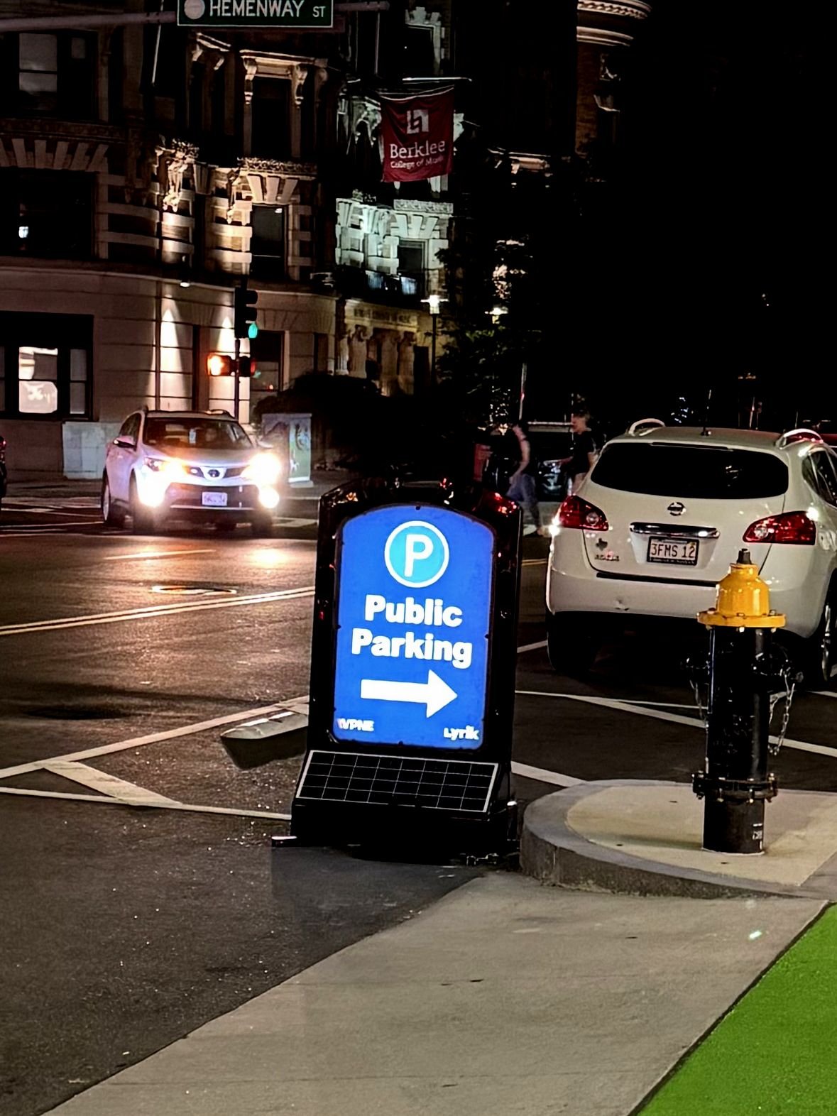 Illuminated sign pointing toward public parking on a city street at night