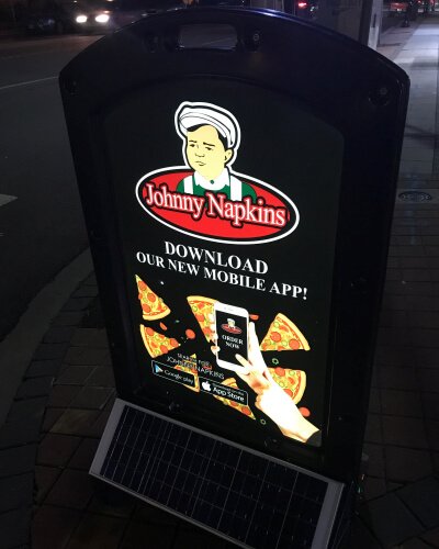 Illuminated sign promoting a restaurant mobile app at night on a sidewalk