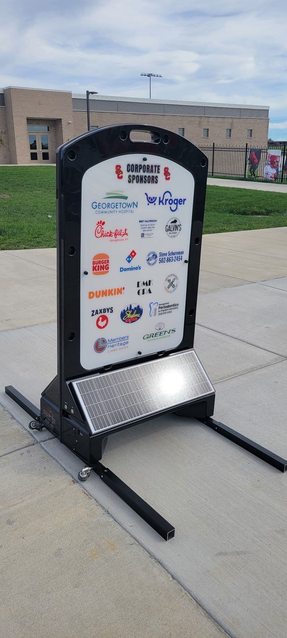 Illuminated sign displaying multiple sponsor logos at a stadium entrance